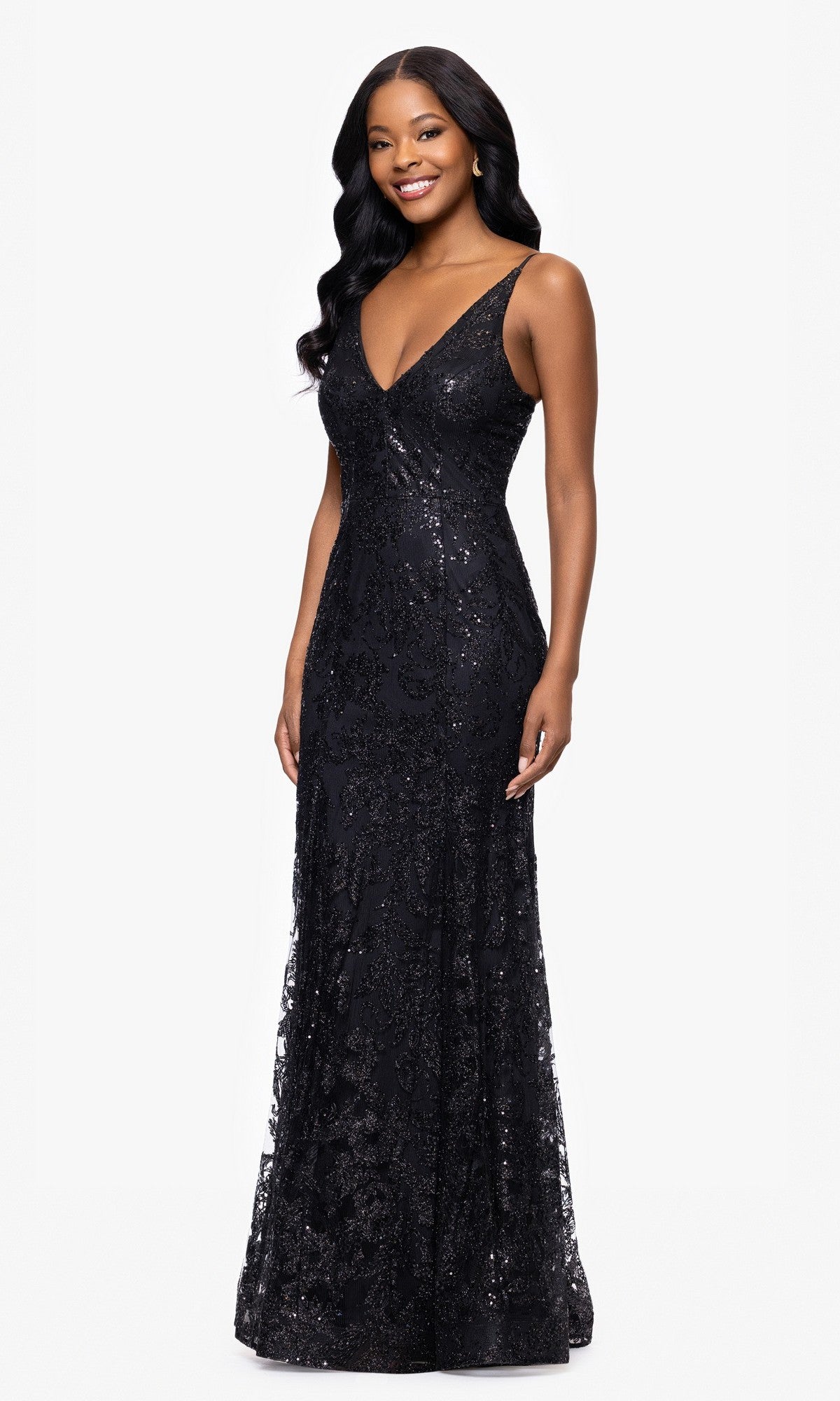 A woman wearing the Blondie Nites 4501BN Long Sequin-Print Prom Dress—a sleeveless, floor-length black gown with strappy back and V-neckline—smiles at the camera against a plain white background.
